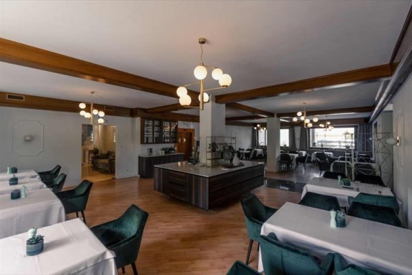 Restaurace s dřevěnými trámy, bílým stropem a židlemi s tmavými potahy.