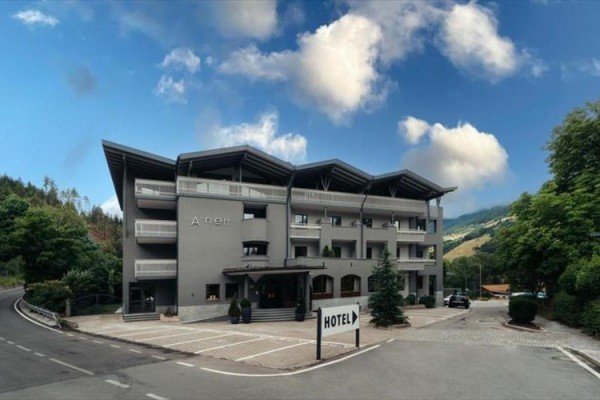 Moderní šedý hotel s balkonem a šikmou střechou obklopený přírodou.