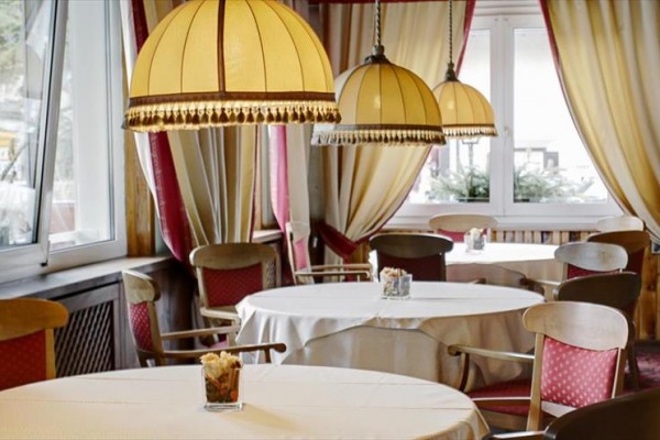 Elegantní restaurace s kulatými stoly, červenými židlemi a velkými lustry s třásněmi.
