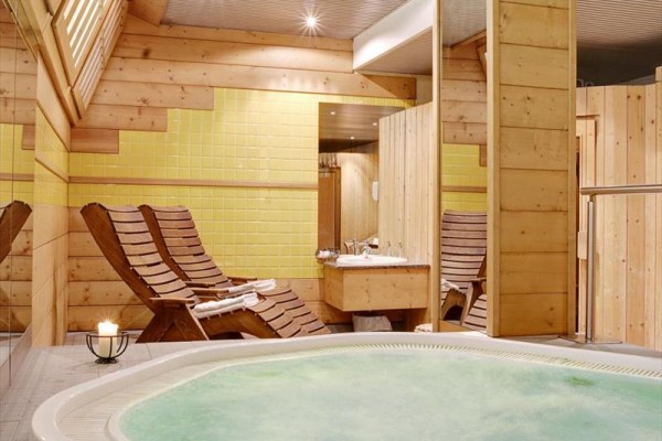 Wellness místnost s vířivkou, dřevěnými lehátky a žlutými dlaždicemi na stěně.