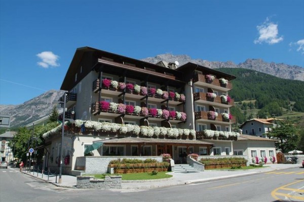 Hotel se zdobenými balkony květinami na pozadí hor a lesa.  