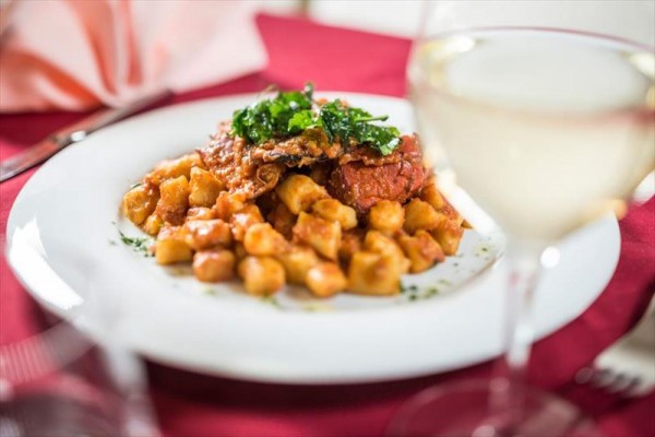Talíř gnocchi s rajčatovou omáčkou a bylinkami na stole s bílým vínem.