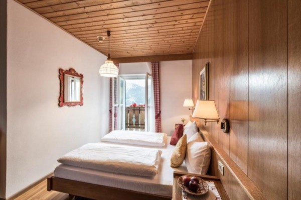Tradiční útulná ložnice s dřevěným stropem, dvojlůžkem a výhledem na balkon s horskou krajinou venku.