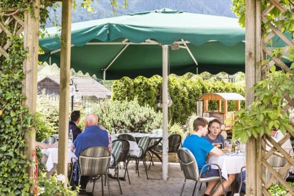 Lidé sedí u stolů pod velkým zeleným slunečníkem v zahradní restauraci.