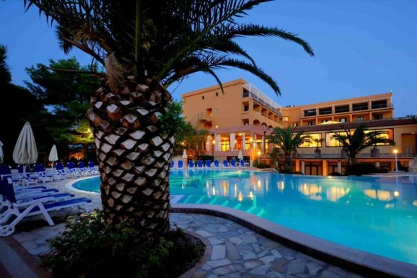 Večerní pohled na hotel s bazénem a palmami.