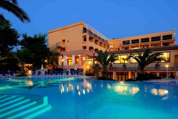 Moderní hotel u osvětleného bazénu s palmami za soumraku.