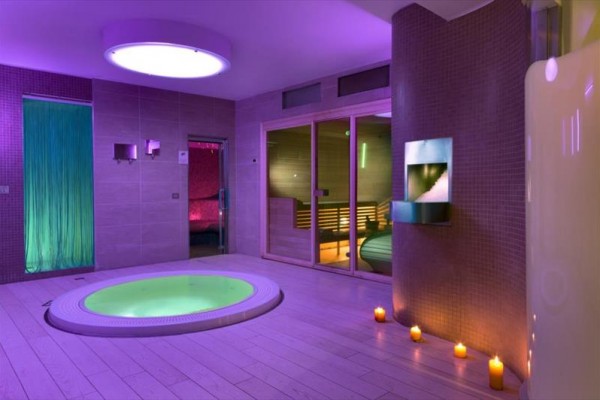 Luxusní spa s vířivkou, saunou a svíčkami při fialovém osvětlení.