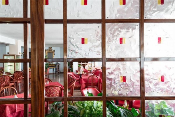 Restaurace oddělená dřevěnou stěnou s prosklenými panely a červenými ubrusy.