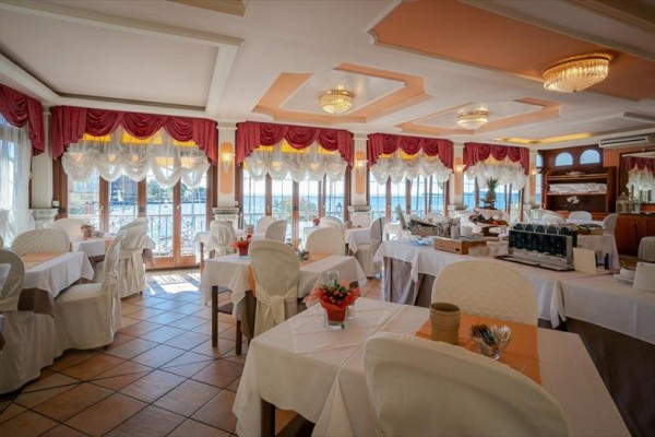 Elegantní prostřená restaurace s bílými ubrusy a červenými závěsy.