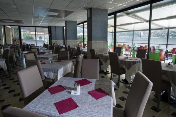 Restaurace s šedými ubrusy a červenými ubrousky u stolů s výhledem na jezero.