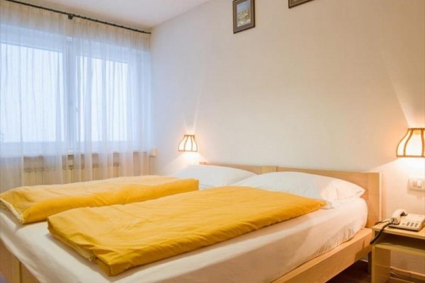 Dvoulůžková postel s žlutým povlečením v pokoji s bílými stěnami a dvěma lampami na nočních stolcích.