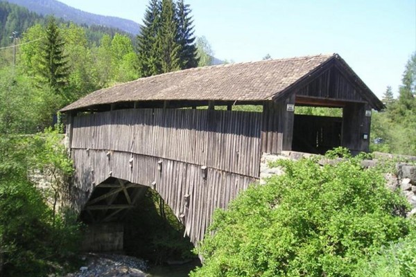 Dřevěný krytý most přes řeku obklopený lesem.