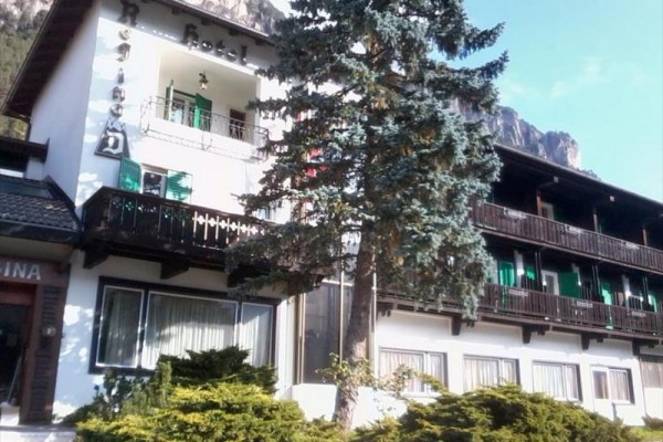 Hotel s balkony a jehličnanem před průčelím.