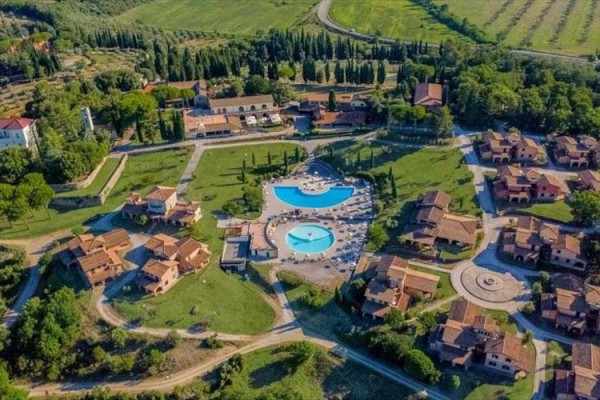 Letovisko s bazény obklopené zelení a domky z ptačí perspektivy.  