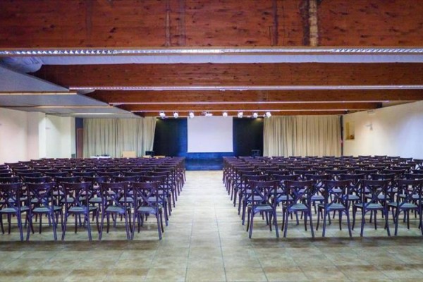 Prázdný konferenční sál se židlemi a projekčním plátnem.