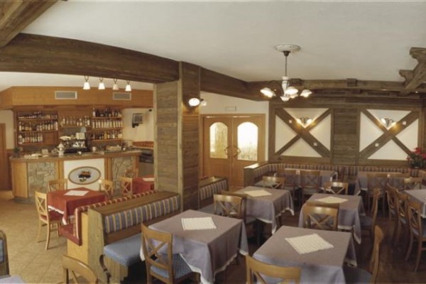 Interiér restaurace s dřevěným nábytkem a barem v pozadí.