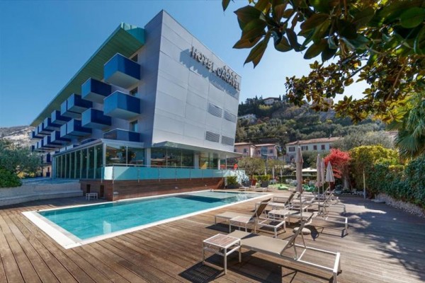 Moderní hotel s venkovním bazénem a lehátky na dřevěné terase.