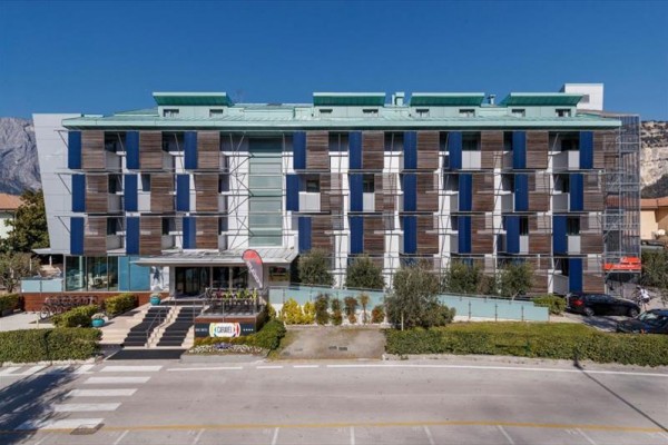 Moderní budova hotelu s modrými a hnědými fasádními prvky, uprostřed městské krajiny.