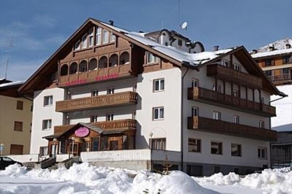 Alpy zasněžený hotel s dřevěnými balkony pod modrou oblohou.