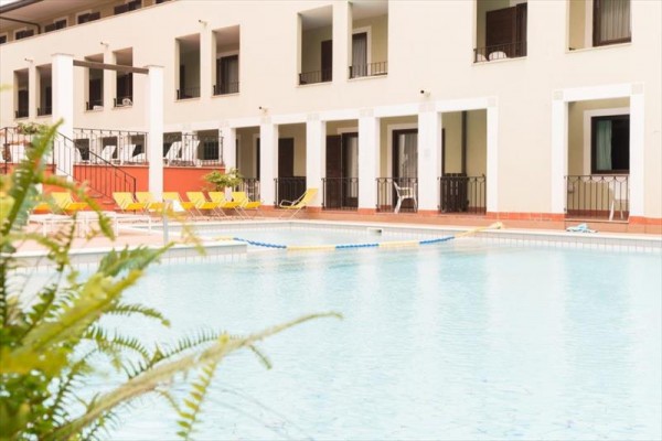 Pohled na plavecký bazén s lehátky před budovou hotelu.