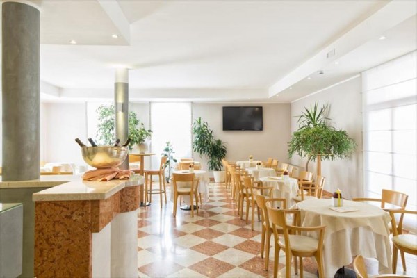 Elegantní restaurace s dřevěnými židlemi a kulatými stoly, ozdobená rostlinami.
