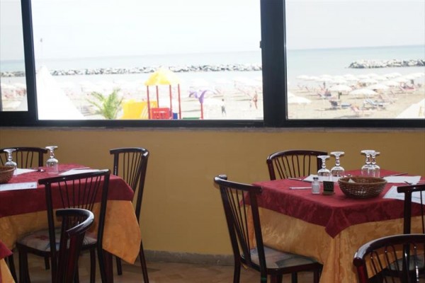 Restaurace s výhledem na pláž s kamenným vlnolamem a slunečníky.