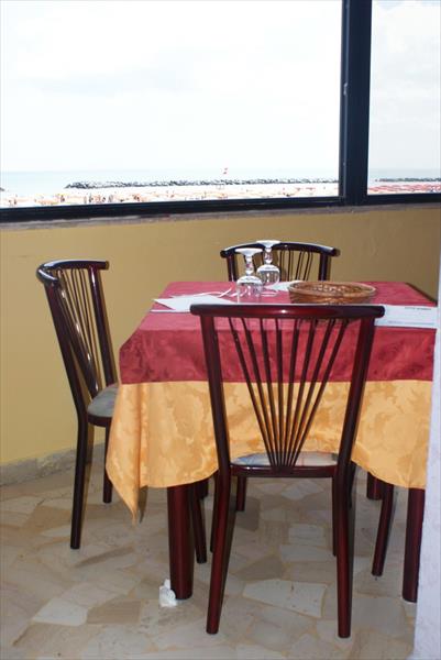 Prosklená restaurace s výhledem na moře a stůl se čtyřmi židlemi pokrytý ubrusem.