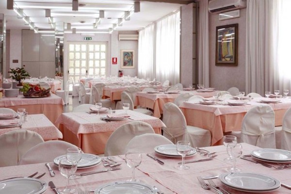 Elegantní restaurace s růžově prostřenými stoly a bílými potahy na židlích.