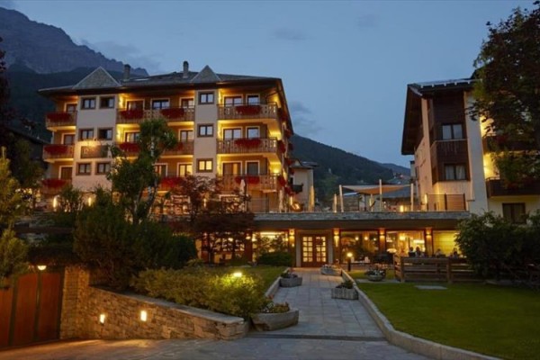 Hotel s osvětlenými balkony v horské oblasti za soumraku.