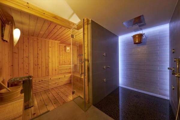 Sauna s dřevěnými lavicemi vedle moderní sprchy.