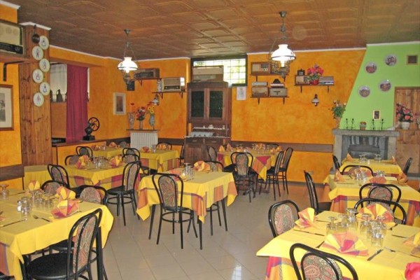 Restaurace s oranžovými stěnami a stoly pokrytými žluto-červenými ubrusy, připravené na hosty. 