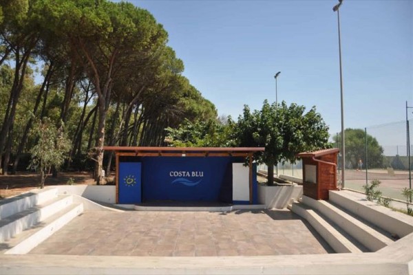 Venkovní prostor s pódium a nápisem Costa Blu obklopený stromy.