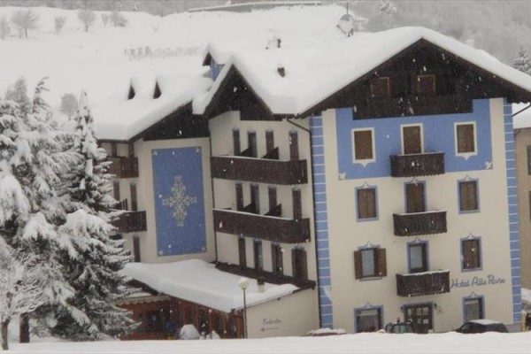 Zasněžený horský hotel s modrými a bílými fasádami a sněhem pokrytou střechou.