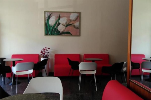 Moderní kavárna s červenými pohovkami, kulatými stoly a obrázkem květin na zdi.