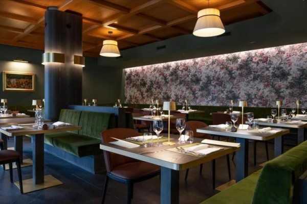 Elegantní restaurace s dřevěným stropem, květinovou tapetou a stolky připravenými na stolování.  