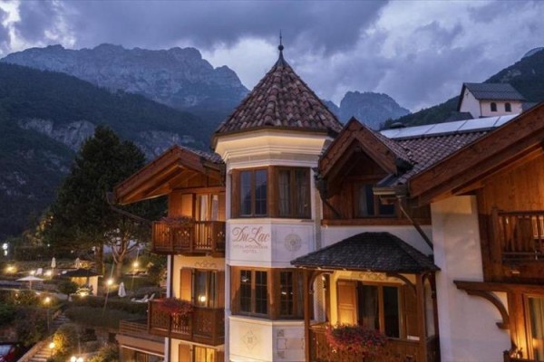 Hotel v alpské krajině za soumraku s osvětlenými okny a horským pozadím.