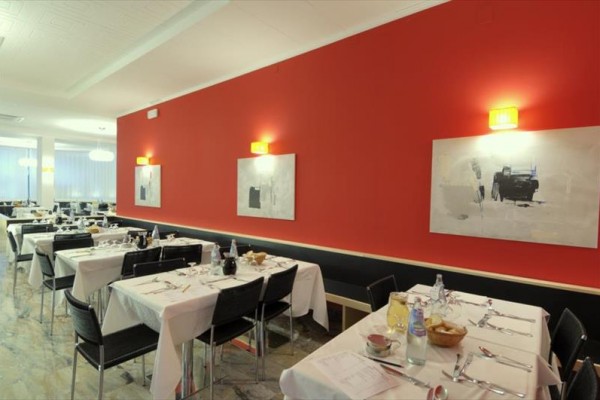 Restaurace s červenou stěnou, prostřenými stoly a moderními obrazy.