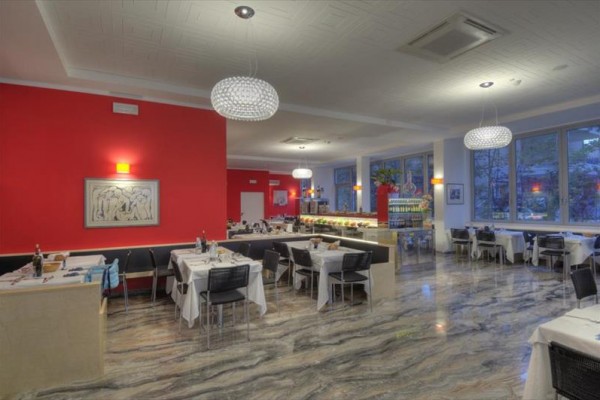 Moderní restaurace s červenými zdmi a elegantními lustry nad prostřenými stoly.