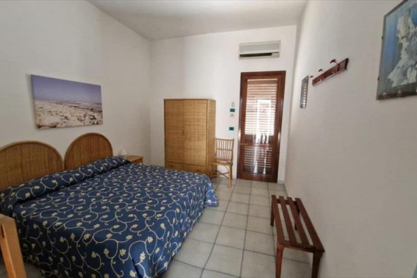 Ložnice s manželskou postelí, dřevěnou skříní a židlí vedle dveří na balkon.