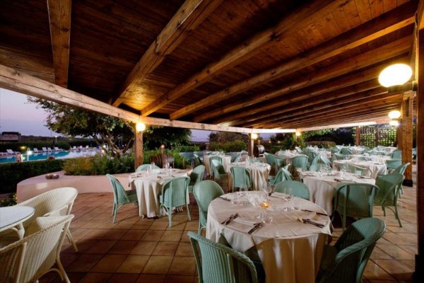 Krytá terasa restaurace s prostřenými kulatými stoly a ratanovými židlemi.