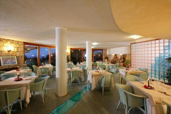 Elegantní restaurace s bílými sloupy, stoly s ubrusy a modrozelenými židlemi.