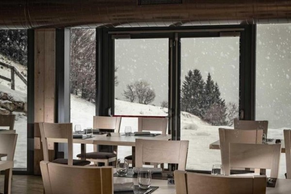 Restaurace s výhledem na zasněženou krajinu skrz prosklené dveře.