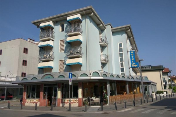Modrý hotel s balkony a markýzou na rohu ulice.