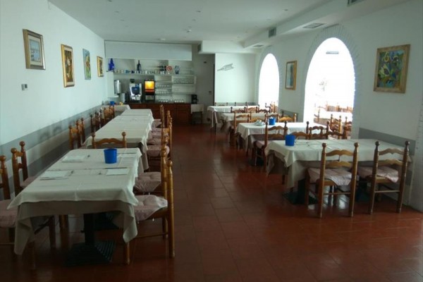 Prázdná restaurace s dřevěnými židlemi a bílými ubrusy na stolech.