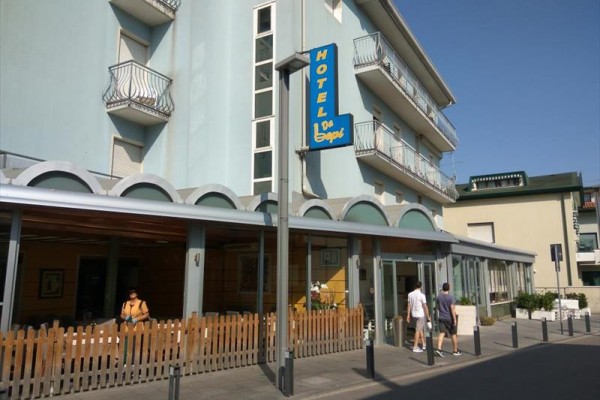 Hotel s modrou fasádou a balkony, vchod s označením 