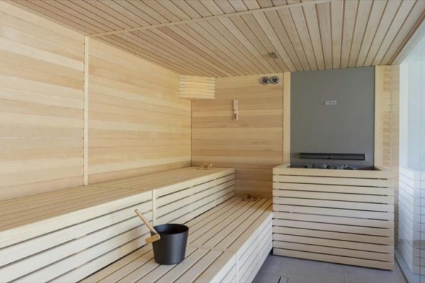 Dřevěná sauna s lavicemi a kamny, v rohu vědro a naběračka na vodu.