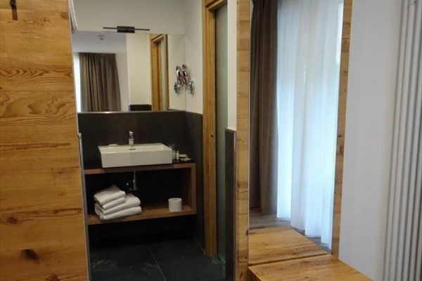 Moderní koupelna s dřevěným prvkem, umyvadlem a velkým zrcadlem.