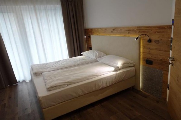 Dvoulůžková postel v moderní ložnici s dřevěnou podlahou a závěsy.