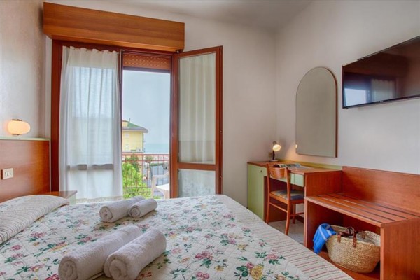 Pokoj v hotelu s manželskou postelí, balkonem a psacím stolem.