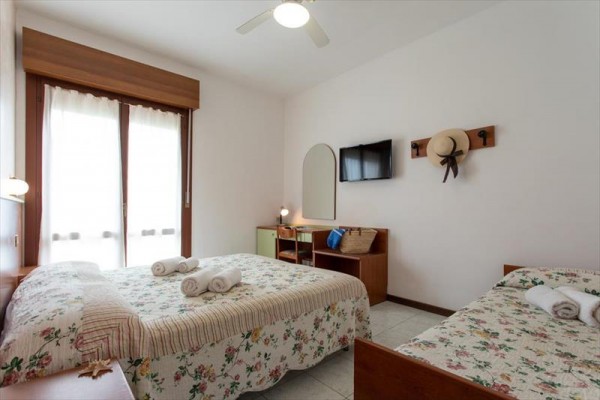 Světlá ložnice s dvěma postelemi, květinovým přehozem, televizí a stropním ventilátorem.